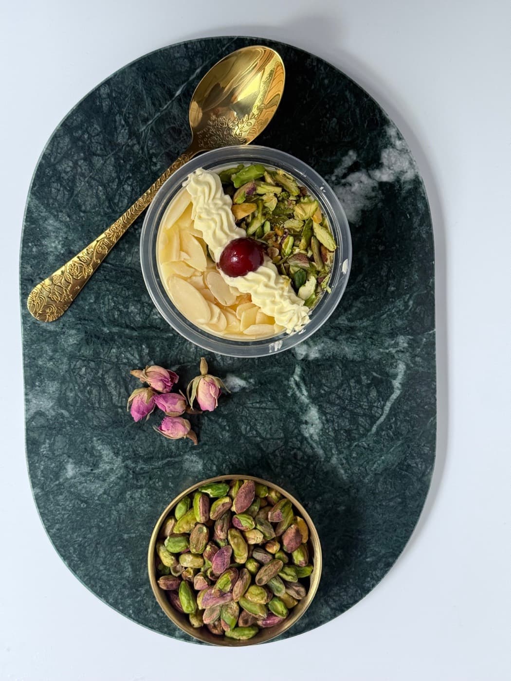 Muhalaya served on a green marble tray with a golden spoon, rose buds and pistachios